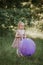 Stylish baby girl 2-5 year old holding big balloon wearing trendy pink dress in meadow. Playful
