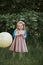 Stylish baby girl holding big balloon wearing trendy pink dress in meadow. Playful. Birthday party