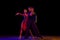 Stylish ballroom dancers couple in gorgeous outfits dancing in sensual pose on dark background in neon light. Concept of