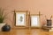 Stylish bamboo frames, potted houseplants and stationery on wooden table near brown wall