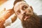 Stylish barber cuts a brutal man with a thick beard.
