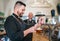 Stylish bearded barman dressed black uniform beer tapping at bar counter and waiter with tray chatting smiling to each other.