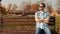 Stylish bearded guy in sunglasses wearing shirt and jeans sits on a bench