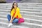 Stylish beautiful girl sitting on a stairs in colorful clothes w