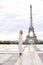 Stylish beautiful woman standing near Eiffel Tower in white overalls.