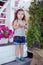 Stylish beautifull cute baby girl with brunette hair posing on wooden garden full of flowers wearing tiny jeans shirts and airy sk