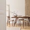 Stylish and beige interior of dining room with design wooden table and chairs, vase with flowers, elegant and rattan accessories.