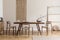 Stylish and beige interior of dining room with design wooden table and chairs, vase with flowers, elegant and rattan accessories.