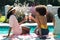 Stylish biracial young females toasting cocktails while having fun pool party during summer