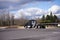 Stylish black big rig semi truck with flat bed semi trailer running on the road with trees and cloudy sky