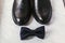 Stylish black shoes and navy bow tie on marble background, top v