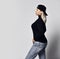 Stylish blonde curvy woman in blue jeans, black turtleneck and cap worn backwards posing