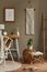 Stylish bohemian interior of home office space with wooden desk, rattan armchair, brown mock up poster frame, macrame, office.