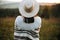 Stylish boho girl posing  in sunny light at atmospheric sunset in meadow. Happy hipster woman in poncho and hat enjoying traveling