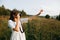 Stylish boho girl taking photo on film analog photo camera of grass and wildflowers in sunny meadow at sunset. Happy hipster woman