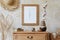 Stylish boho interior of living room with brown mock up poster frame, elegant accessories, flowers in vase, wooden shelf.