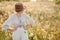 Stylish boho woman in hat posing among wildflowers in sunset light. Summer delight and travel. Young female in rustic linen cloth