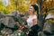 Stylish bride with a rustic bouquet is posing before a lake on the hill. Young blonde in a knitted hat with pompom and