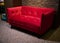 Stylish bright red upholstered velour sofa, displayed for sale in a furniture showroom interior lit with soft dim light, against