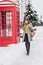 Stylish british image of fashionable young woman walking on street in winter time near red telephone box. Talking on