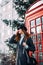 Stylish British portrait of a charming young woman brunette in a fashionable cap walking down the street near the red phone booth