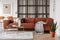 Stylish brown corner sofa with patterned pillows in elegant living room interior with mullions wall