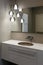 Stylish brown sink, chrome faucet, large mirror and ceiling light three-lamp chandelier. Modern bathroom design