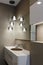 Stylish brown sink, chrome faucet, large mirror and ceiling light three-lamp chandelier. Modern bathroom design