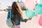 Stylish brunette girl with colofrul balloons walking down the street enjoys sunny day. Young curly woman wearing denim