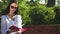 Stylish brunette in sunglasses read the book on a bench in park