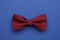 Stylish burgundy bow tie with polka dot pattern on blue background, top view
