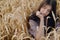 Stylish calm woman sitting in wheat field in evening light. Atmospheric tranquil moment. Young female in rustic linen dress