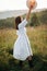 Stylish carefree boho girl throwing her hat in the sky in sunny light  at atmospheric sunset. Happy hipster woman in linen rustic