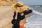 Stylish carefree woman in hat walking on sunny beach at sea and enjoying summer vacation. Young female in straw hat and light