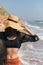 Stylish carefree woman in hat walking on sunny beach at sea and enjoying summer vacation. Young female in straw hat and light