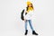 Stylish caucasian charming girl in a white shirt, blue jeans, a yellow hat, with a backpack on his shoulders posing on a