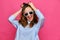 Stylish caucasian girl in a pale blue t-shirt and 8-bit glasses grabs hair and smiles on a pink background