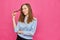 Stylish caucasian girl in a pale blue t-shirt looks dissatisfied and twists hair on a finger on a pink background