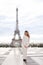 Stylish caucasian girl standing near Eiffel Tower in white overalls.