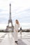 Stylish caucasian woman standing near Eiffel Tower in white overalls.