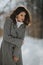 Stylish Caucasian woman wearing a coat with a houndstooth pattern in a forest covered in the snow