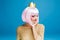 Stylish charming young woman with cut pink hair on blue background. Golden sweater, crown on head, smiling with closed