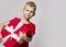 Stylish cheerful boy child in red t-shirt holding big present box with ribbon in hands looking at camera