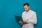 Stylish cheerful and positive businessman in a white shirt works in a laptop on a blue background