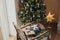 Stylish christmas gifts in festive wrapping paper with bows, vintage ornaments, toy on chair on background of golden christmas