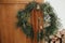 Stylish christmas rustic wreath with vintage bells and ribbon on brass handle on wooden doors close up. Winter holiday decoration
