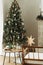 Stylish christmas tree, wooden table with christmas gift and candle, rustic decorated fireplace in modern farmhouse. Atmospheric
