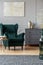 Stylish coffee table next to emerald green armchair in trendy living room interior with grey design