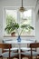 Stylish composition of dining room interior with design table, chairs, tropical leaf in vase, window and elegant decoration.