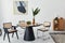 Stylish composition of dining room interior with design table, modern chairs, decoration, tropical leaf in vase, fruits, bookcase.